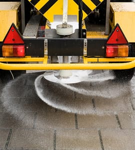 A machine is sprinkling salt on a sidewalk